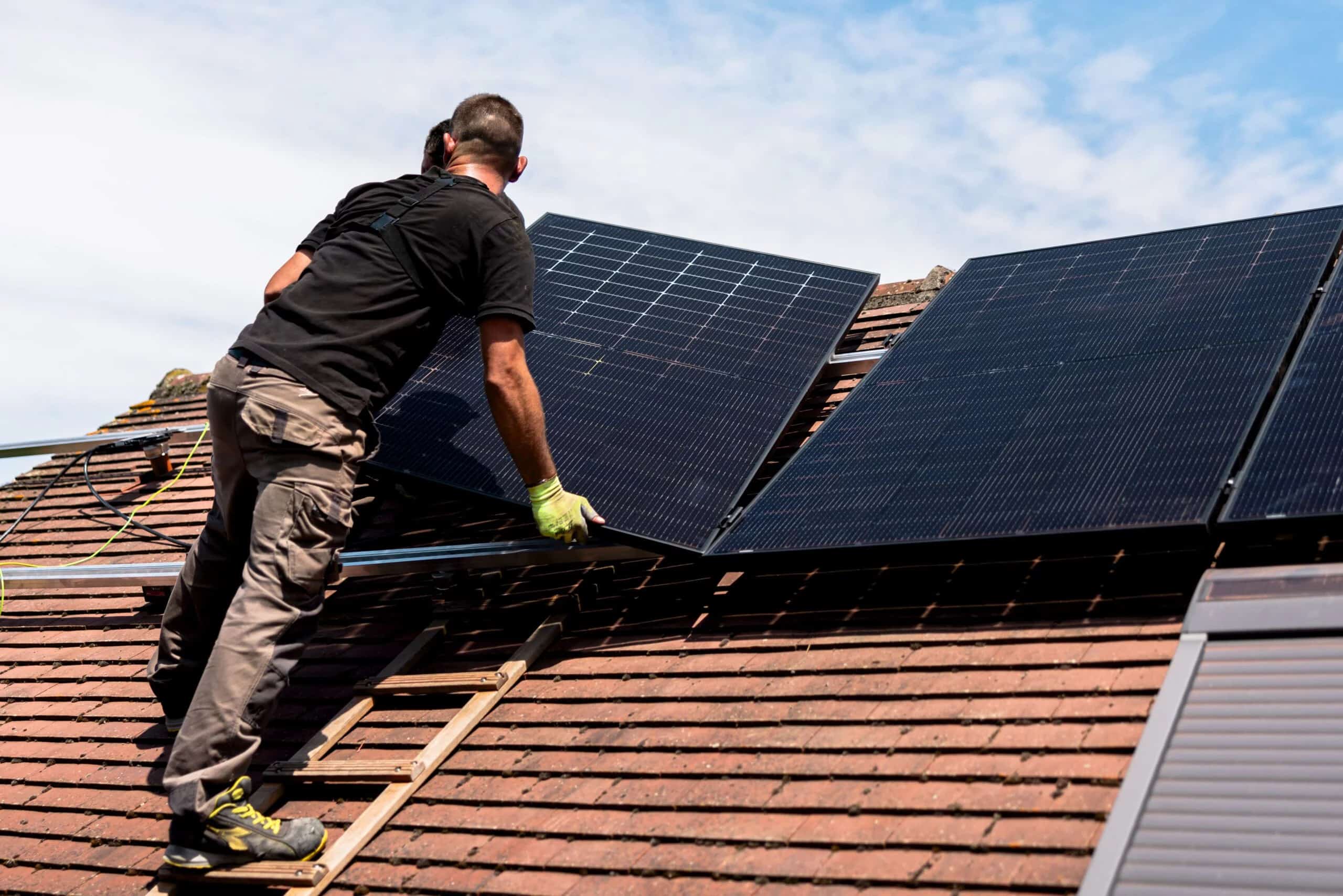 Un homme sur le toit installe un panneau photovoltaique. La durée de vie d'un onduleur joue un rôle dans le fonctionnement du système photovoltaique.